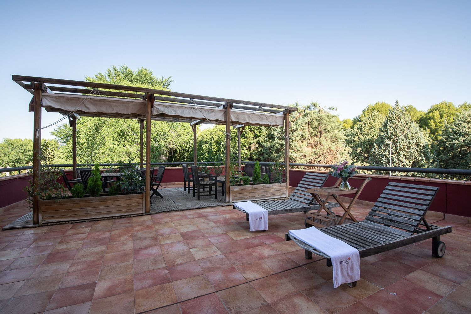 Une terrasse sur le toit, aménagée avec des meubles en bois, une pergola et offrant une vue sur les arbres.