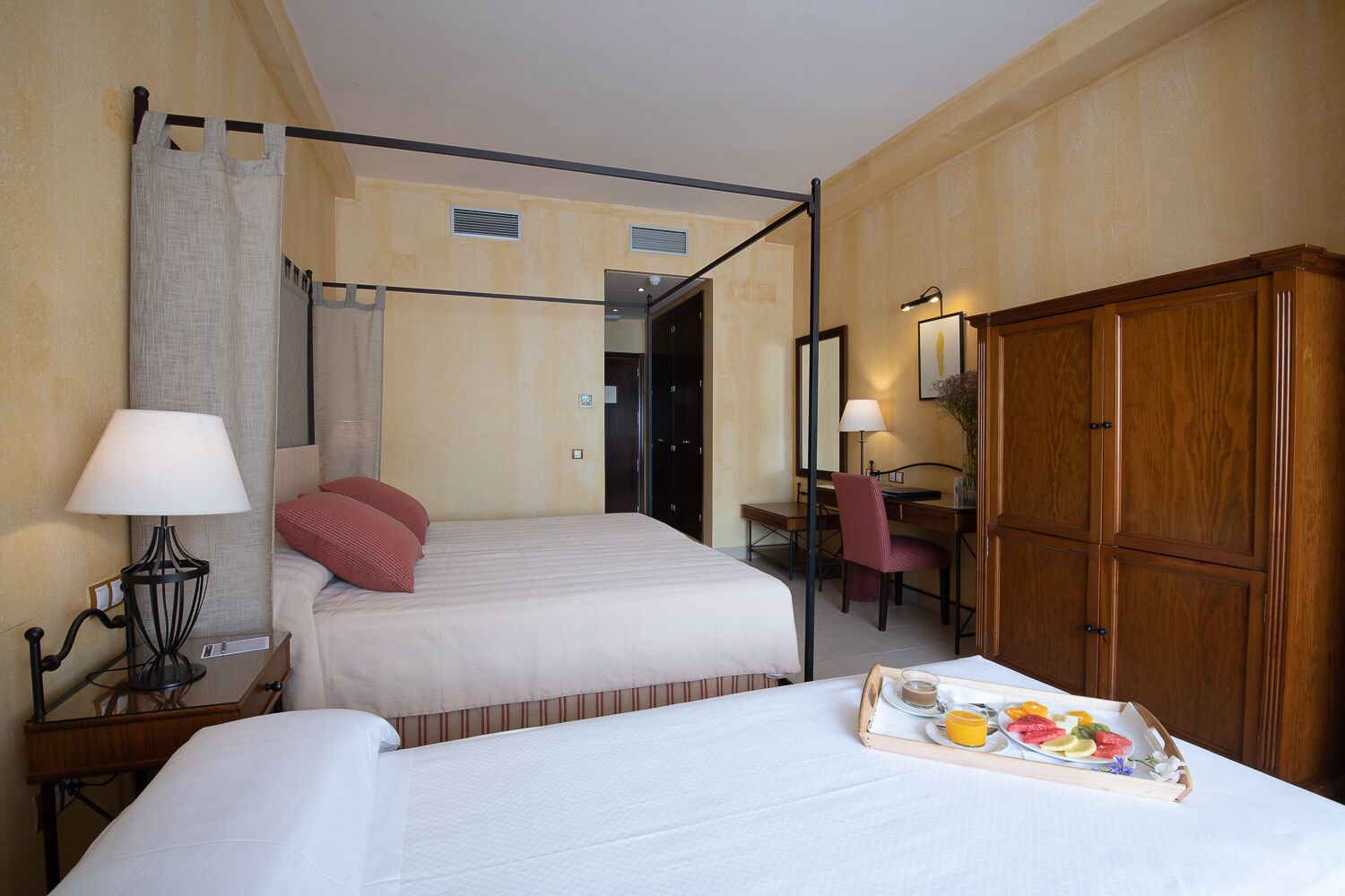 A hotel room with a bed, a desk, a wardrobe, and a tray of breakfast.