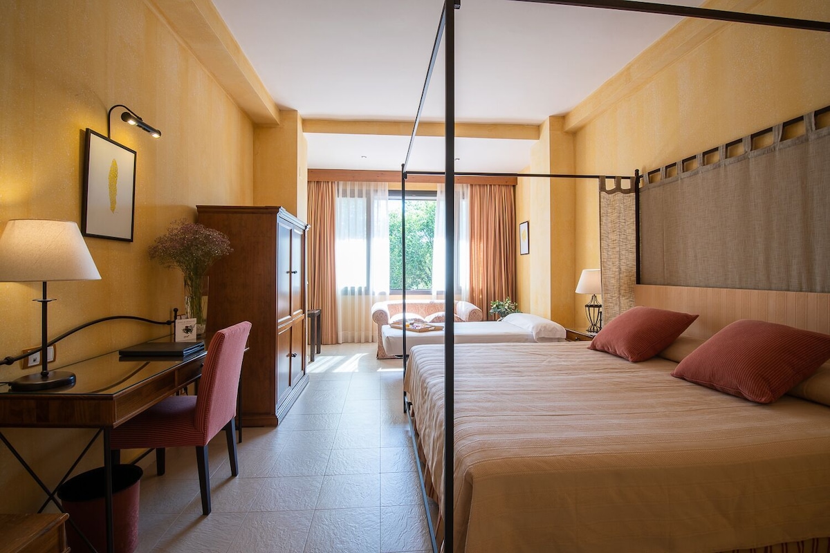 Habitación de hotel con cama, escritorio, silla y vistas al exterior.