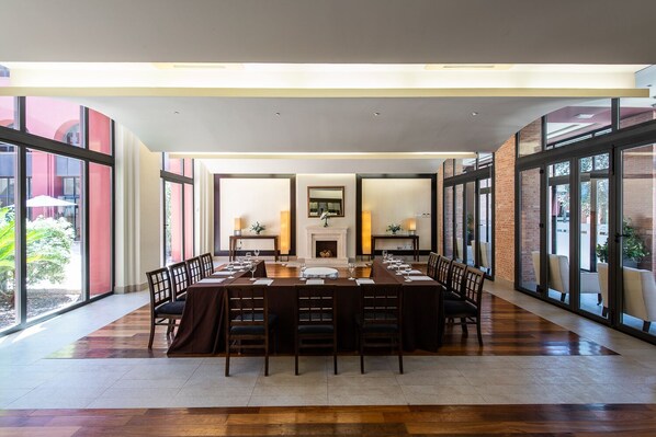 A spacious dining area with a long table set for a meal, large windows, and a fireplace.
