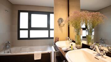 A modern bathroom with a freestanding bathtub, two sinks, a large mirror, and a window with blinds.