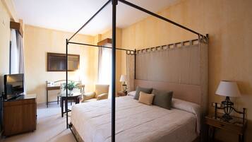 Una cama con dosel y tablero de cabecera, un televisor, un escritorio con silla y una mesita de noche con lámpara.