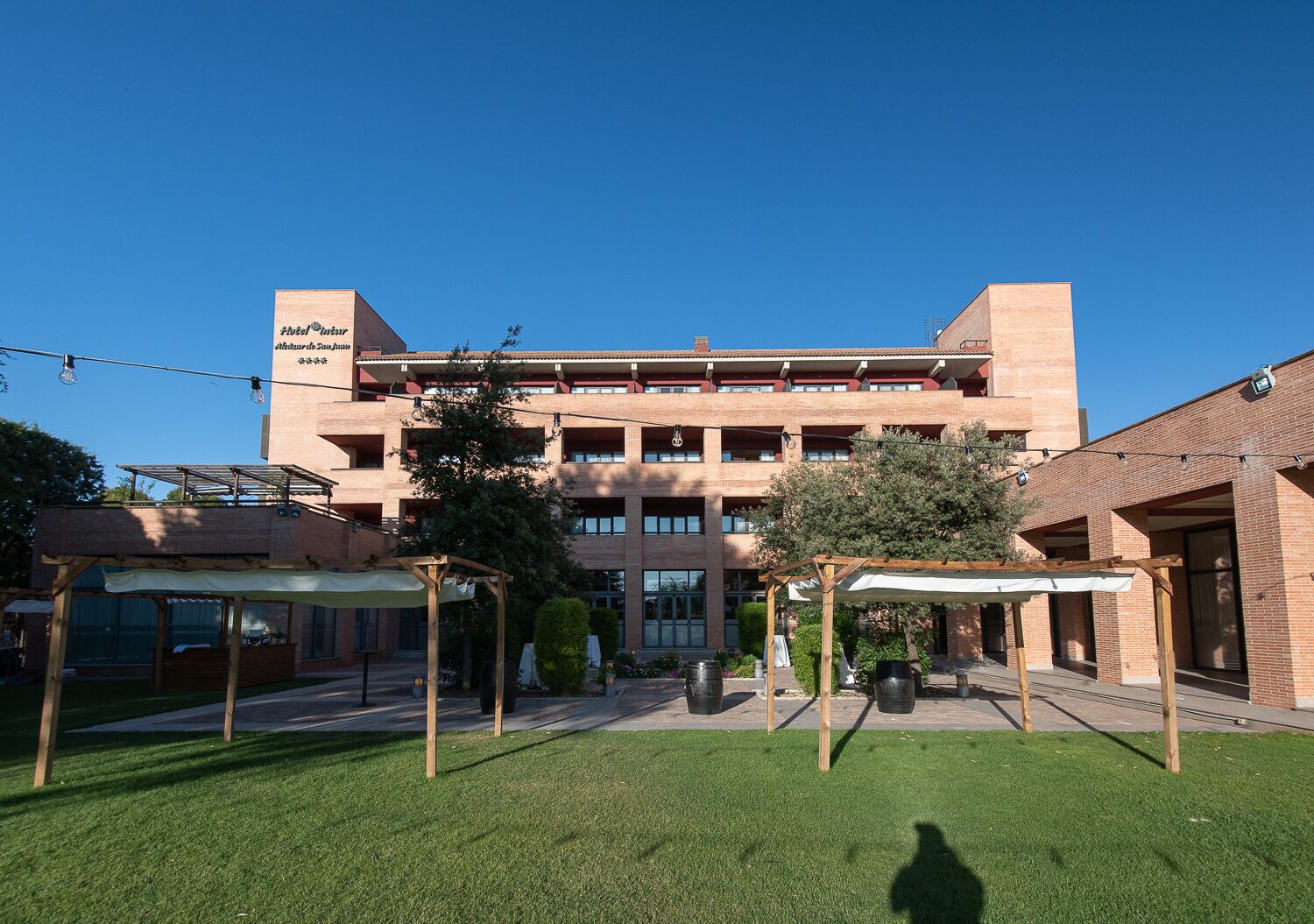 A multi-story hotel with a brick facade, outdoor seating areas, and a well-maintained lawn.