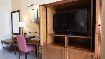Habitación de hotel con un mueble de madera que contiene una televisión de pantalla plana, un escritorio con una silla, una lámpara y un cuadro en la pared.