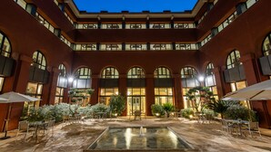 A courtyard with a central fountain, surrounded by outdoor seating and plants, and a building with multiple floors and large windows. - Intelier Airén Hotel by Intelier Hotels & Suites (Alcazar de San Juan)
