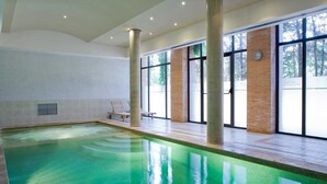 An indoor swimming pool with clear water, large windows, and a brick wall. - Intelier Airén Hotel by Intelier Hotels & Suites (Alcazar de San Juan)
