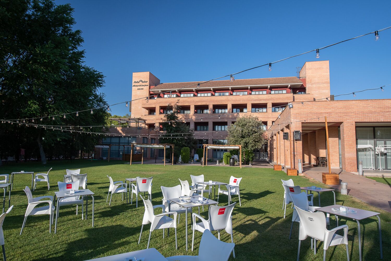 Un patio de hotel con mesas al aire libre y un edificio de ladrillo al fondo.