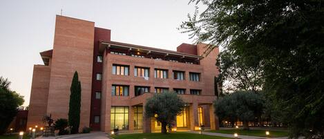 Un edificio de varios pisos con fachada de ladrillo, ventanas grandes y un césped bien cuidado con árboles.