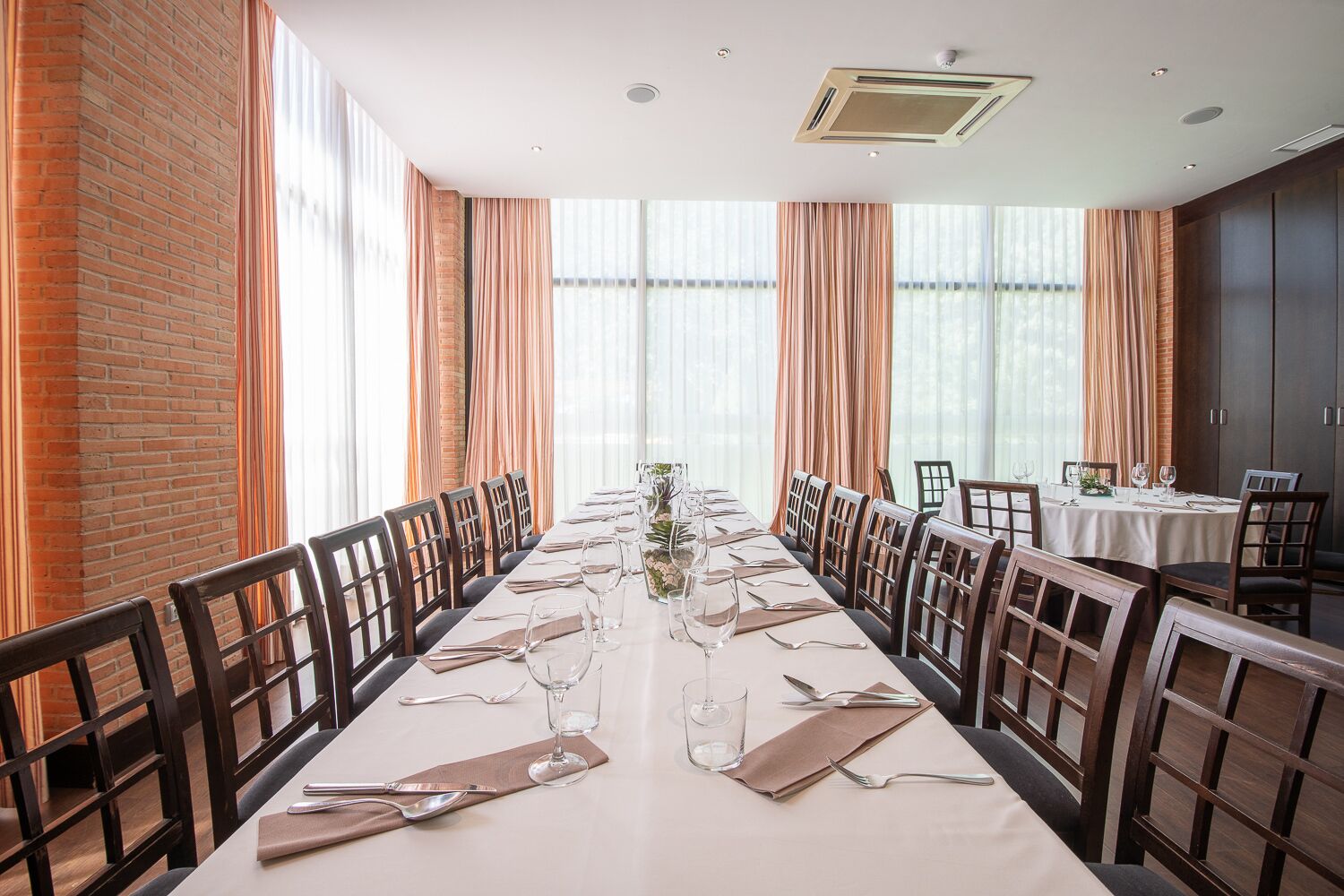 A long dining table set for a meal in a room with brick walls and large windows.