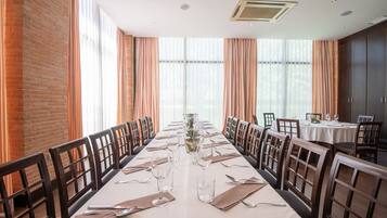 Una larga mesa de comedor lista para una comida en una habitación con paredes de ladrillo y ventanas amplias.