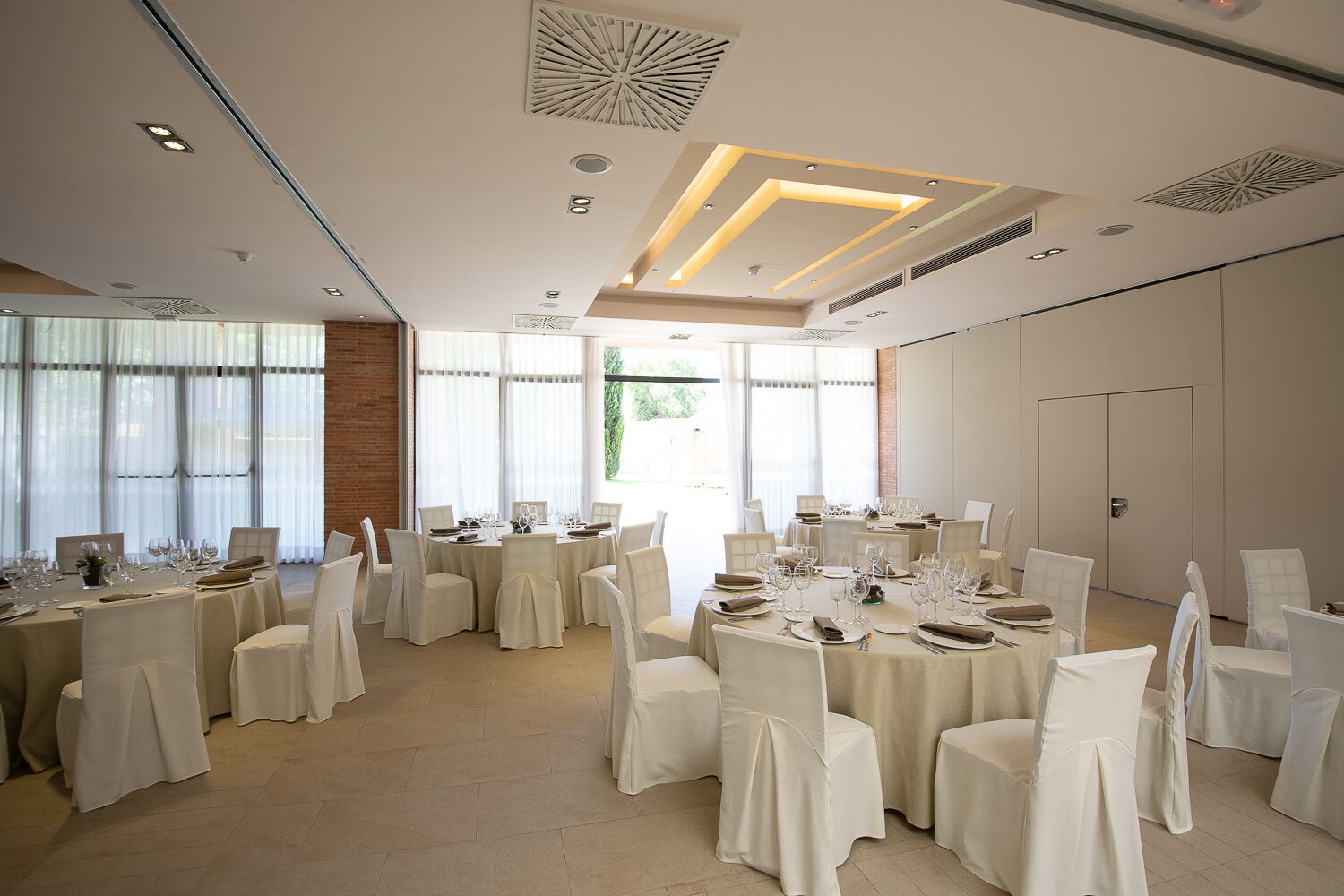A spacious banquet hall with multiple round tables set for dining, featuring white tablecloths and chairs.
