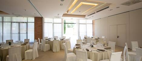 A spacious banquet hall with multiple round tables set for dining, featuring white tablecloths and chairs.
