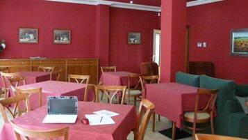 A dining area with red walls, wooden tables, and chairs. There are framed pictures on the walls and a laptop on one table.
