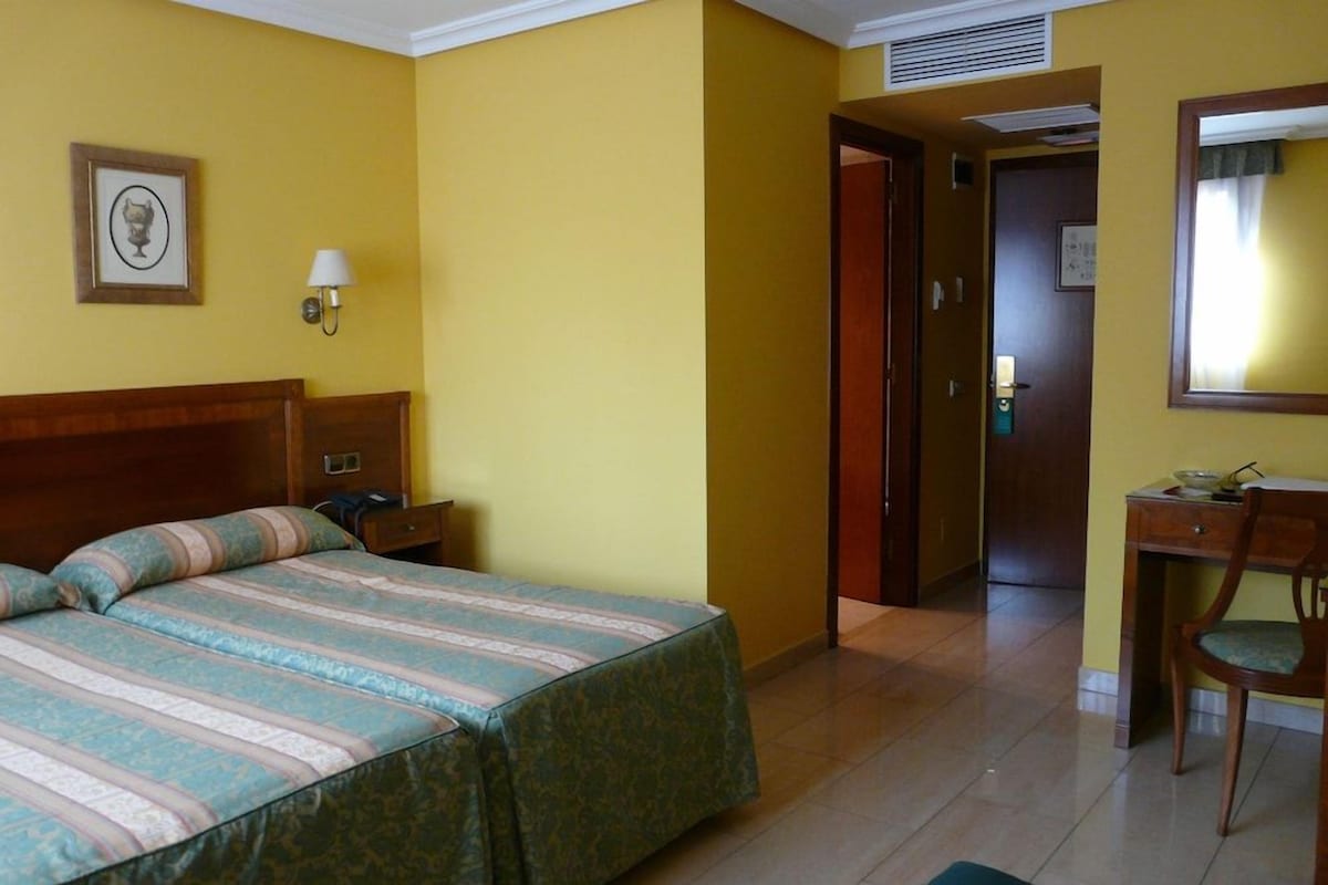 Una habitación de hotel con cama, mesita de noche, lámpara y escritorio con silla.