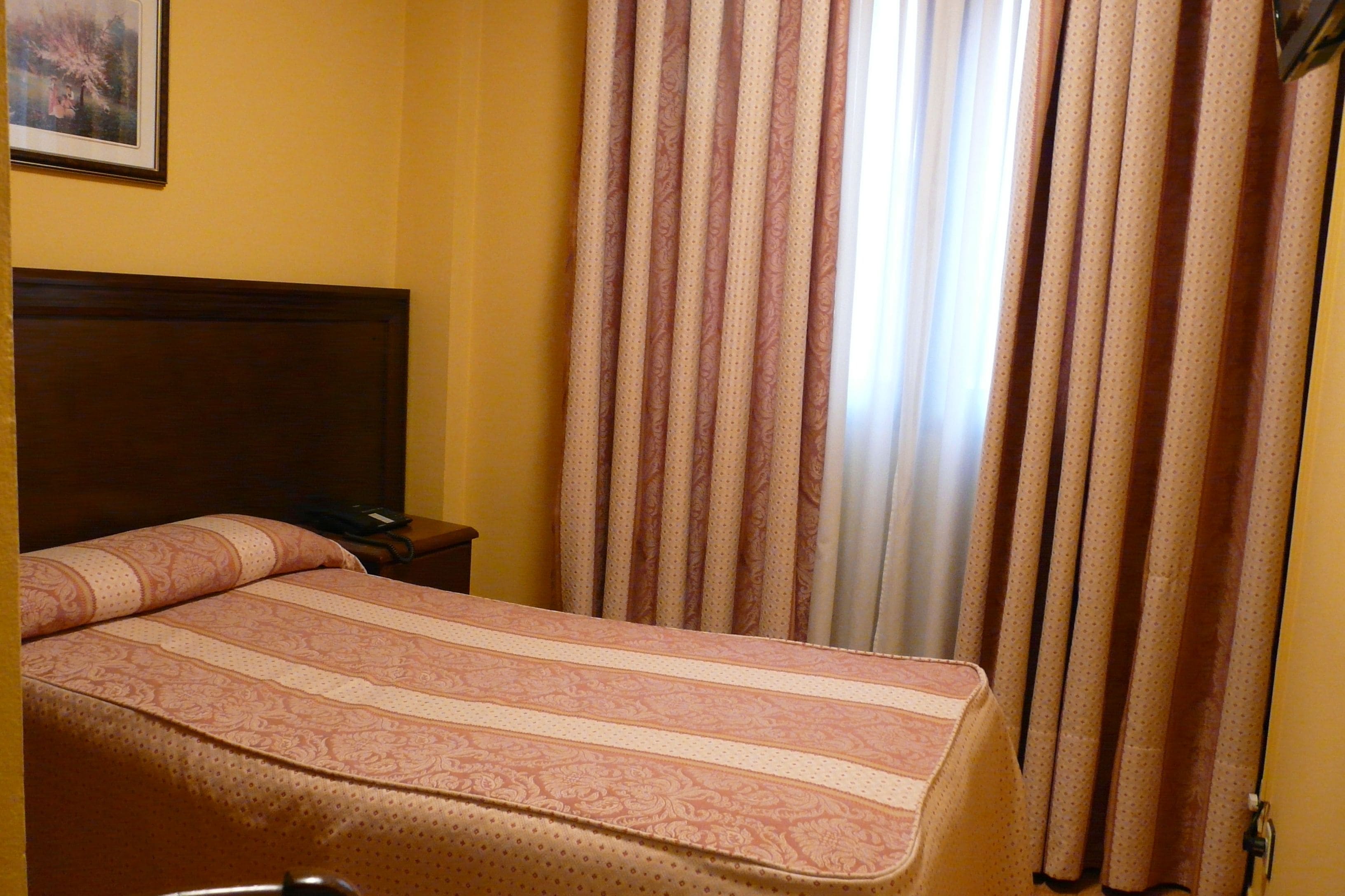 Una habitación de hotel con una cama, una mesita de noche y cortinas.