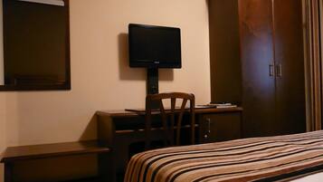 Una camera d'albergo con un letto, una scrivania, una sedia, una televisione e un armadio.
