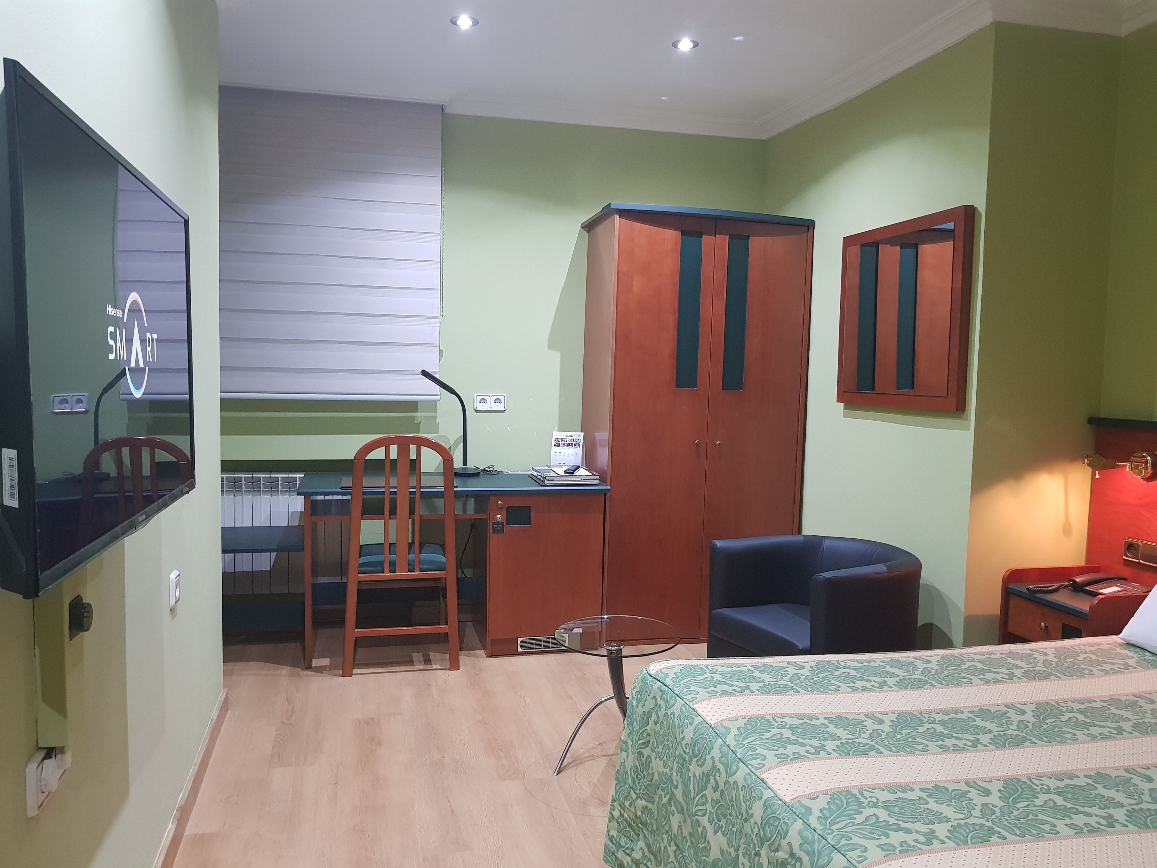 A room with a bed, desk, chair, wardrobe, and a television.