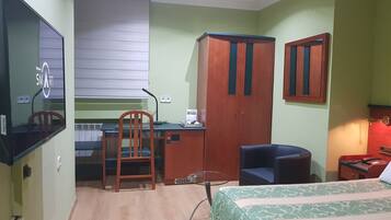 A room with a bed, desk, chair, wardrobe, and a television.