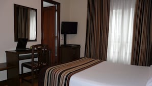 Una habitación de hotel con una cama, un escritorio con una computadora portátil, una silla, un televisor y cortinas.