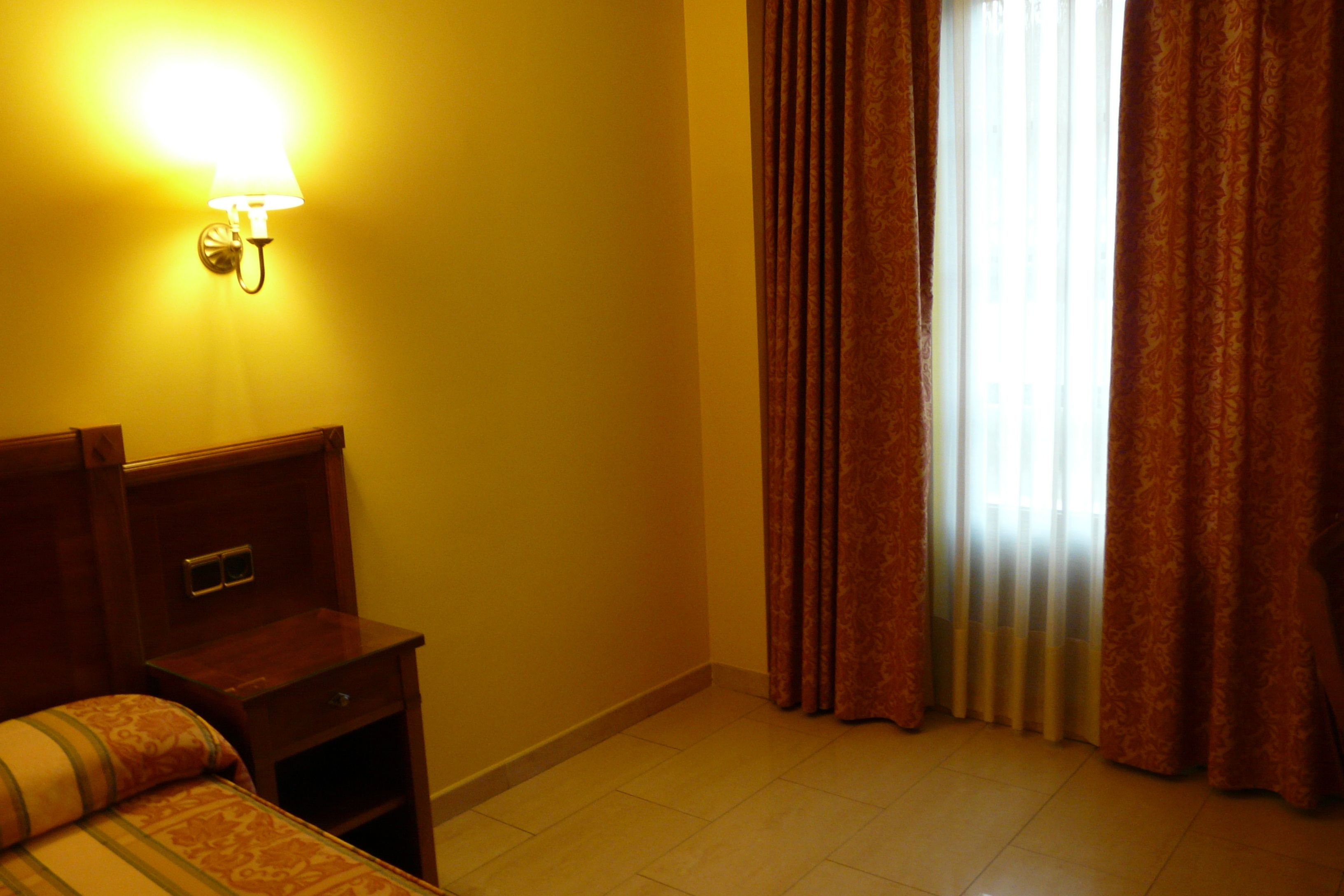 A hotel room with a bed, a nightstand, a lamp, and a window with curtains.