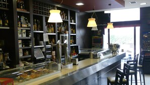 Un bar con estantes llenos de botellas, una caja registradora y taburetes.