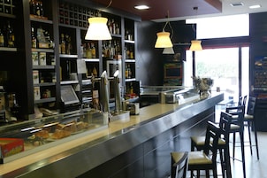 Um balcão de bar com prateleiras cheias de garrafas, um caixa registradora e banquetas.
