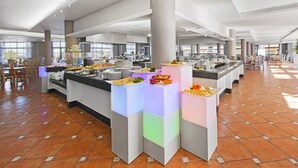 Un comedor de hotel amplio con múltiples estaciones de buffet, un pilar central y suelo de baldosas.