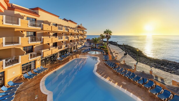 Un resort con piscina, tumbonas y vista al mar.