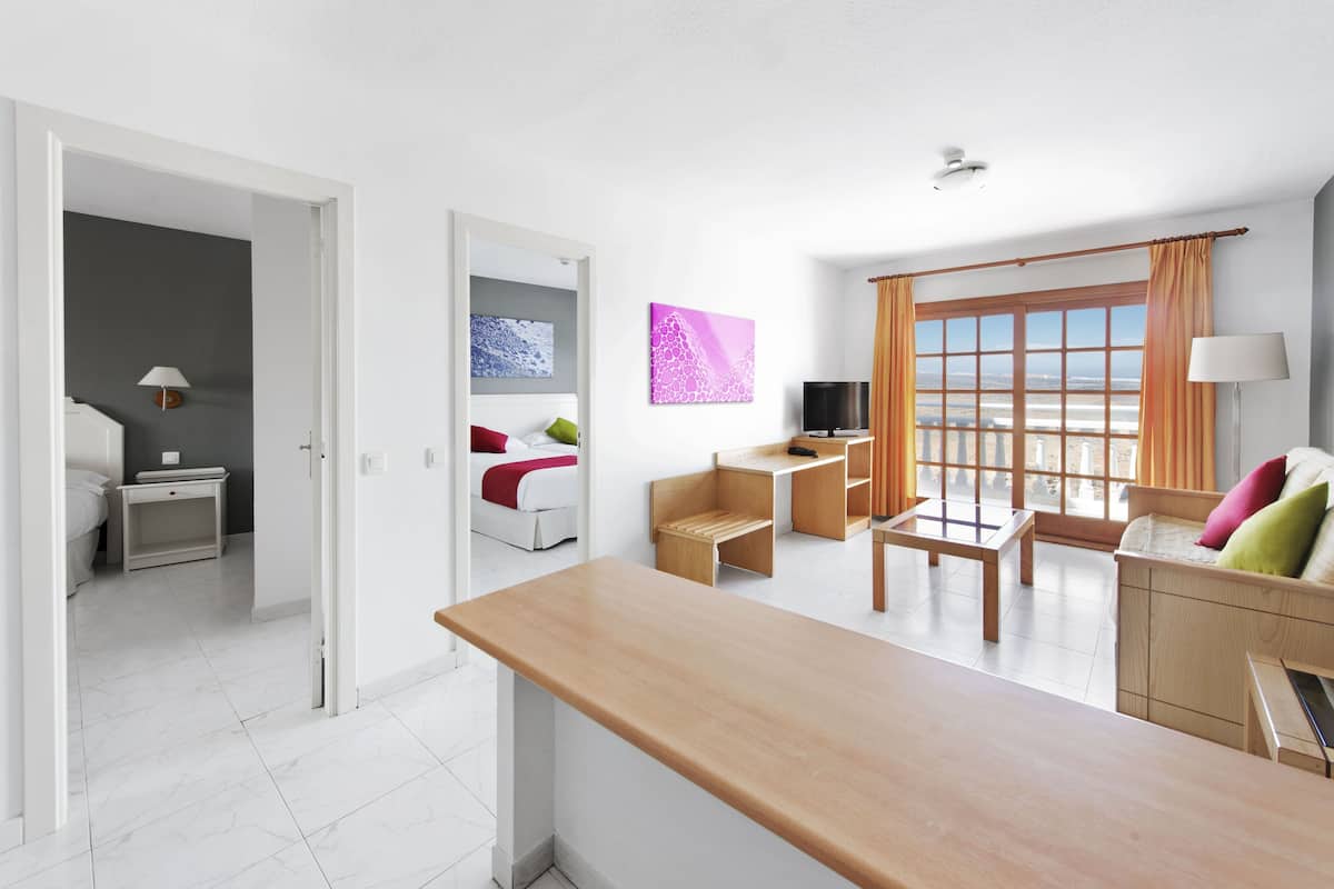 Una habitación de hotel moderna con un escritorio de madera, un sofá, un televisor y un balcón con cortinas.