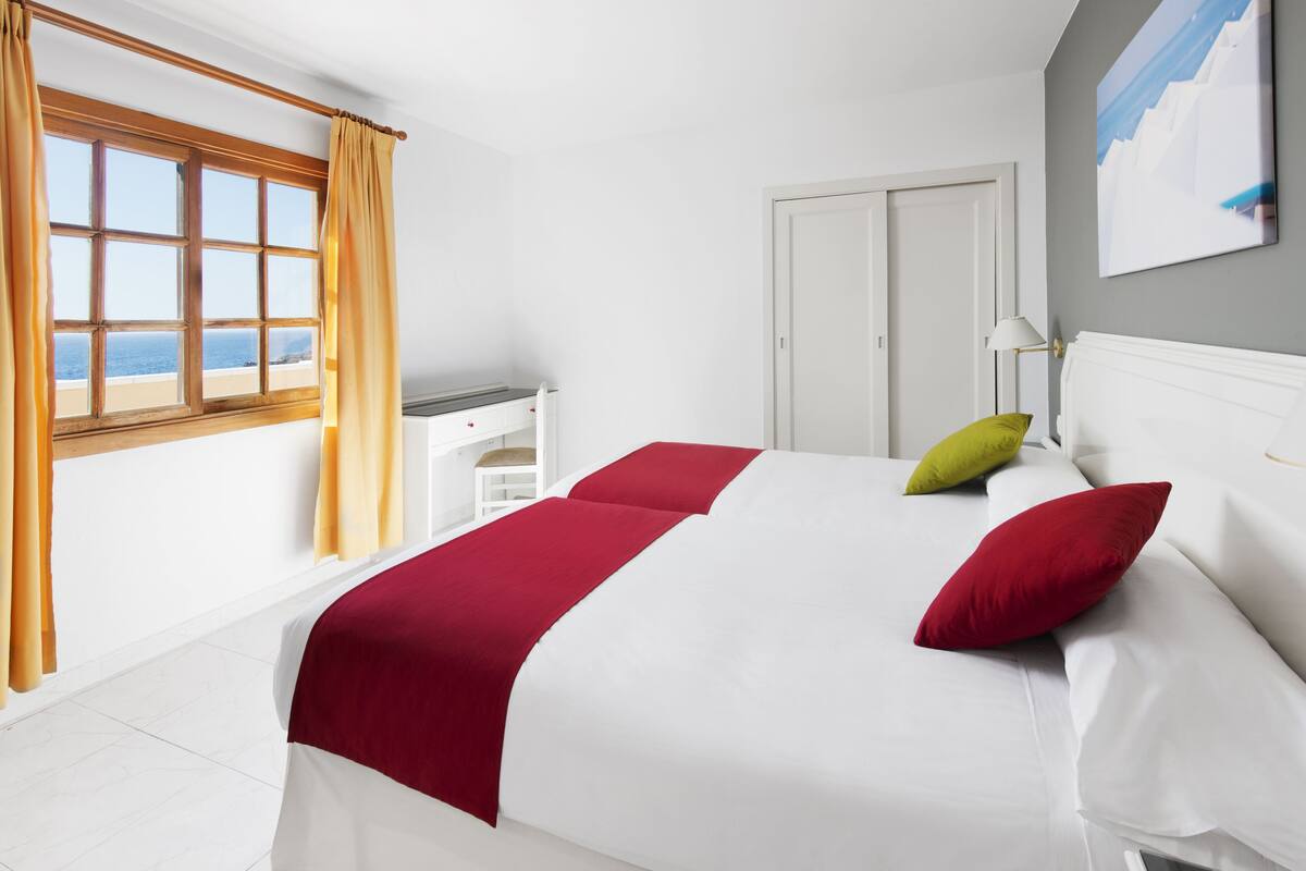 Habitación de hotel con cama, escritorio, silla, armario y vistas al mar.