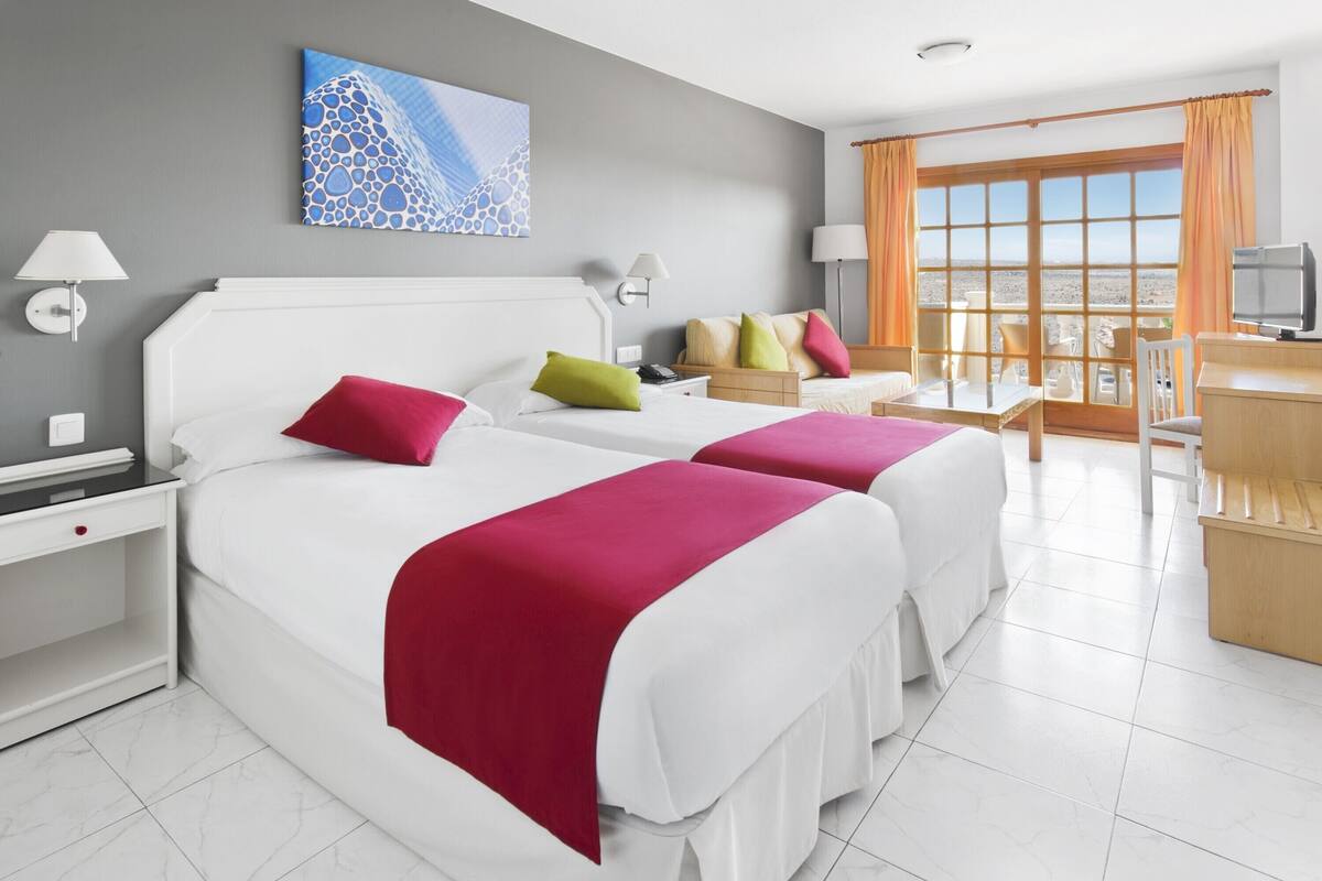 Habitación de hotel con dos camas, un escritorio y vista a la playa.