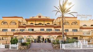 Un hotel con varios balcones, una entrada central con escalones y una palmera en primer plano.