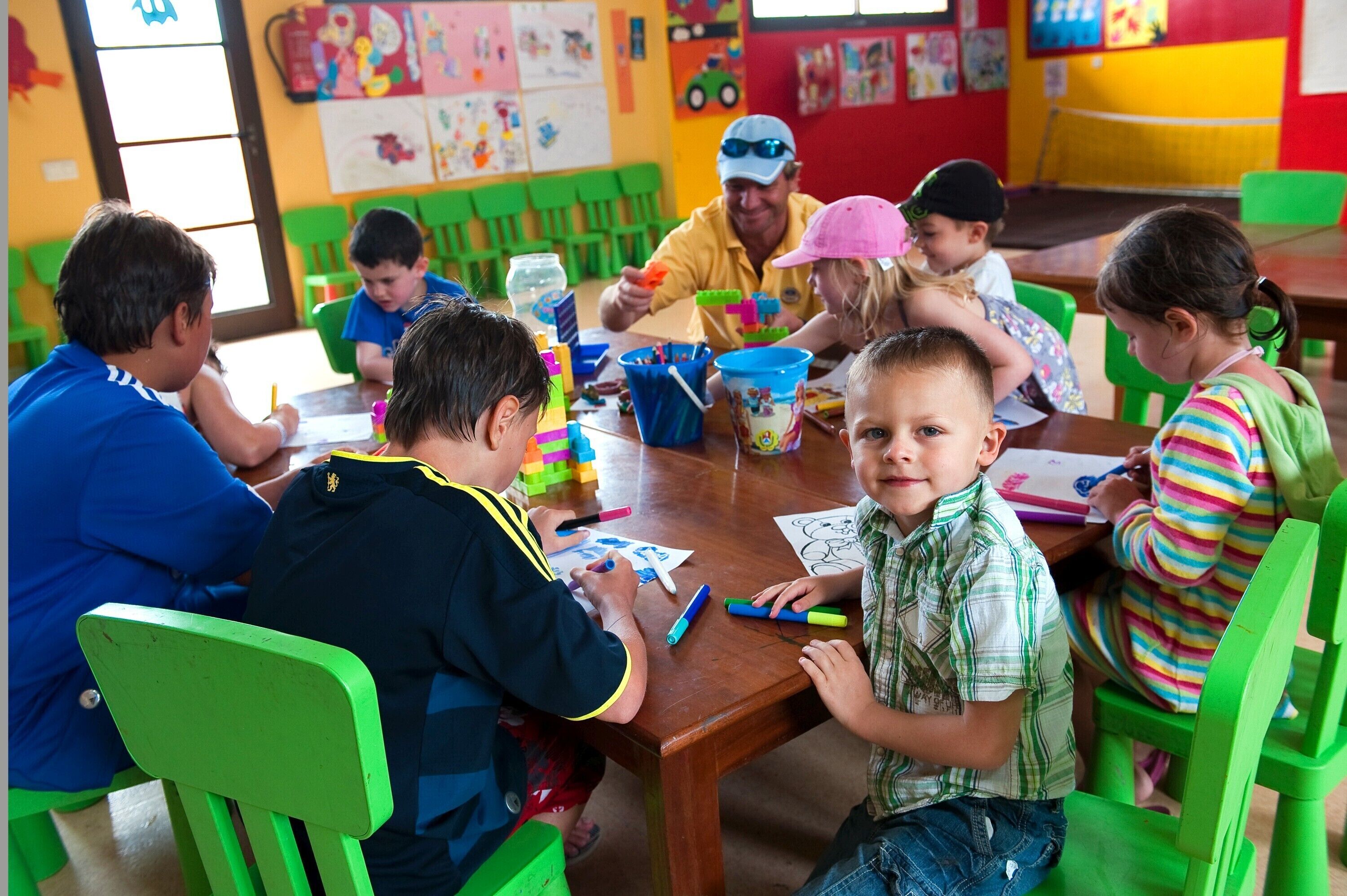 A classroom with children engaged in activities, green chairs, and educational materials on the table.