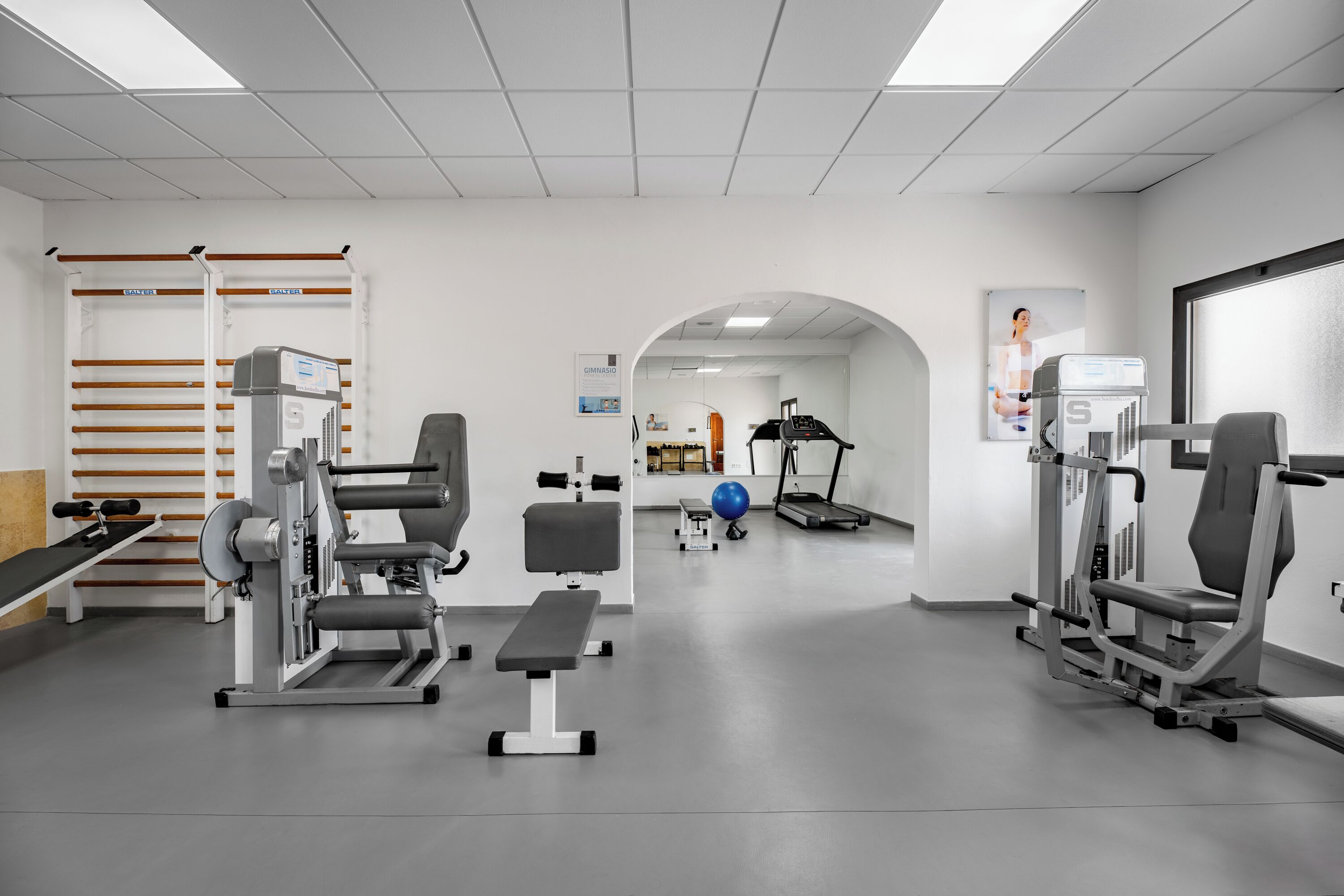 Un gimnasio con equipo de ejercicio, una banca y una cinta de correr.