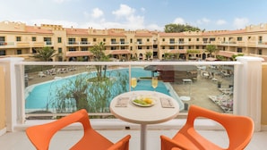 Ein Balkon mit orangefarbenen Stühlen, einem Tisch mit Essen und Blick auf einen Pool sowie Hotelgebäude.