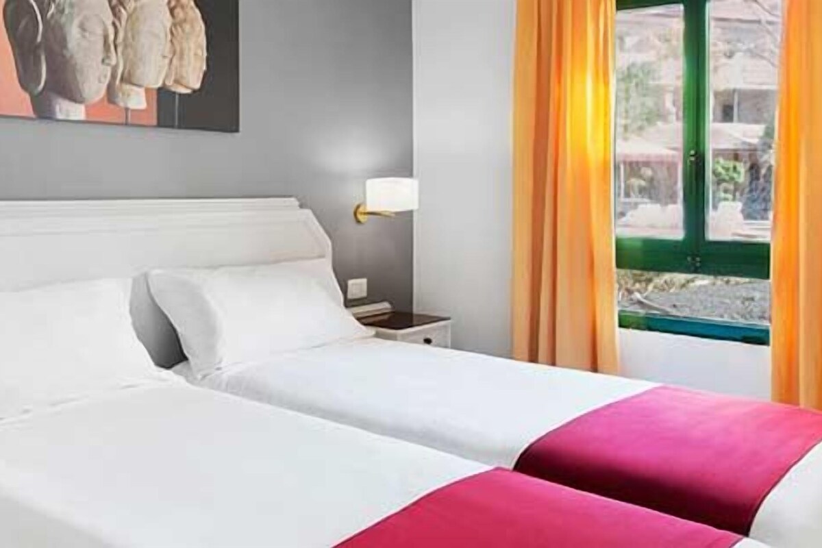 A hotel room with a bed, bedside tables, and a window with curtains.