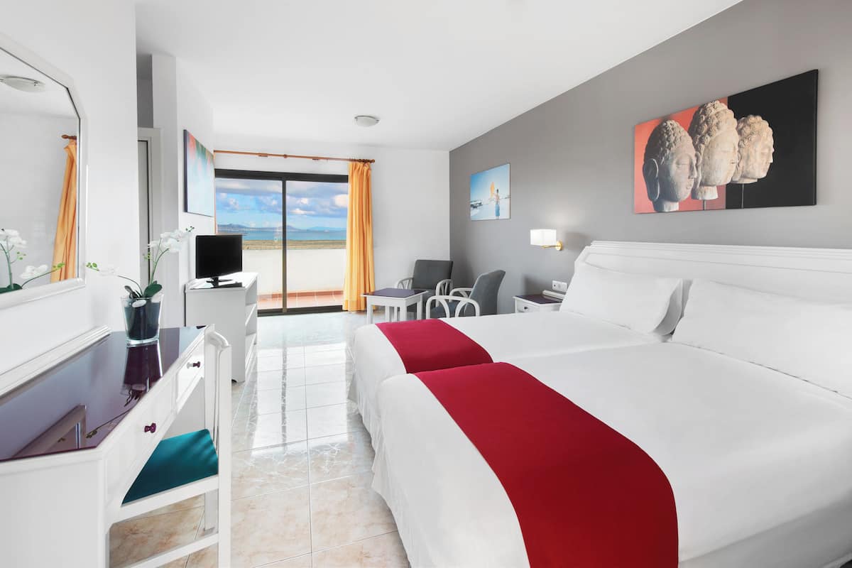 A hotel room with a bed, desk, chair, and a view of the sea.