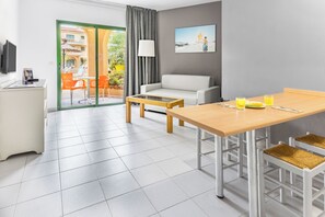 A modern hotel room with a dining area, a sofa, a flat-screen TV, and a view of the outdoors. - Elba Lucía Sport & Suite Hotel (Antigua)