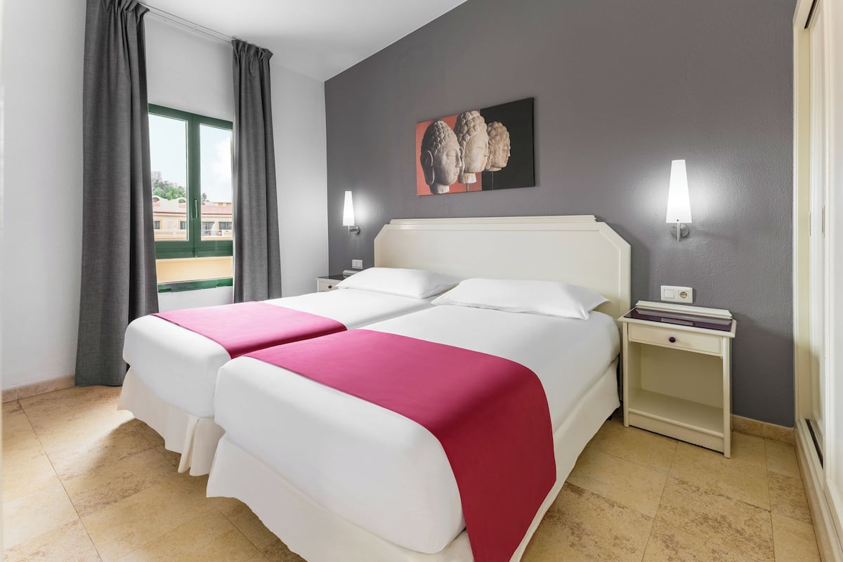 A double bed with white and pink bedding, a nightstand with a lamp, and a painting on the wall.