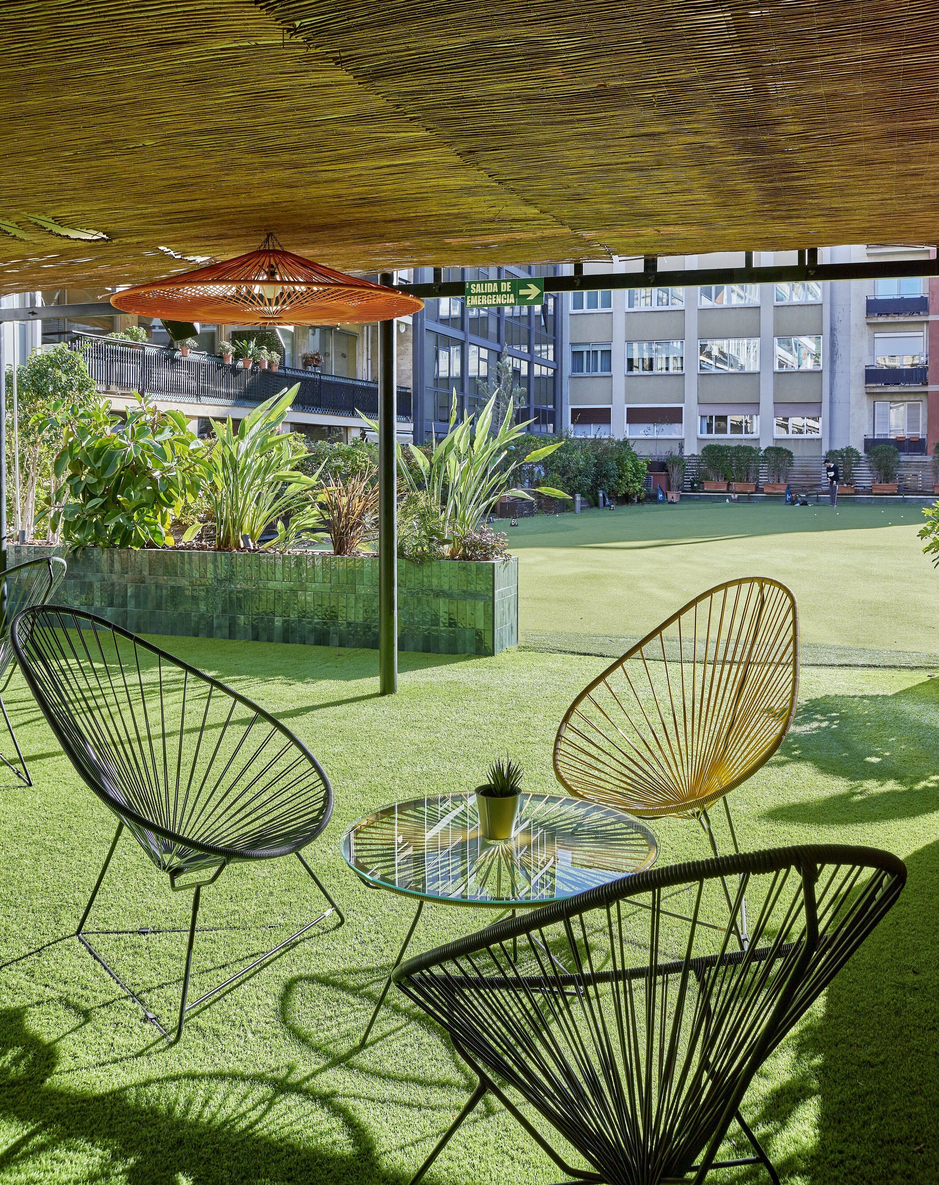 Un espace extérieur aménagé avec des chaises et une table, entouré d’une pelouse verdoyante et de plantes en pot.