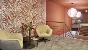 A modern hotel lobby with a patterned wallpaper, a round table with a vase of flowers, two armchairs, and a staircase with a railing. - The Moods Oasis (Barcelona)