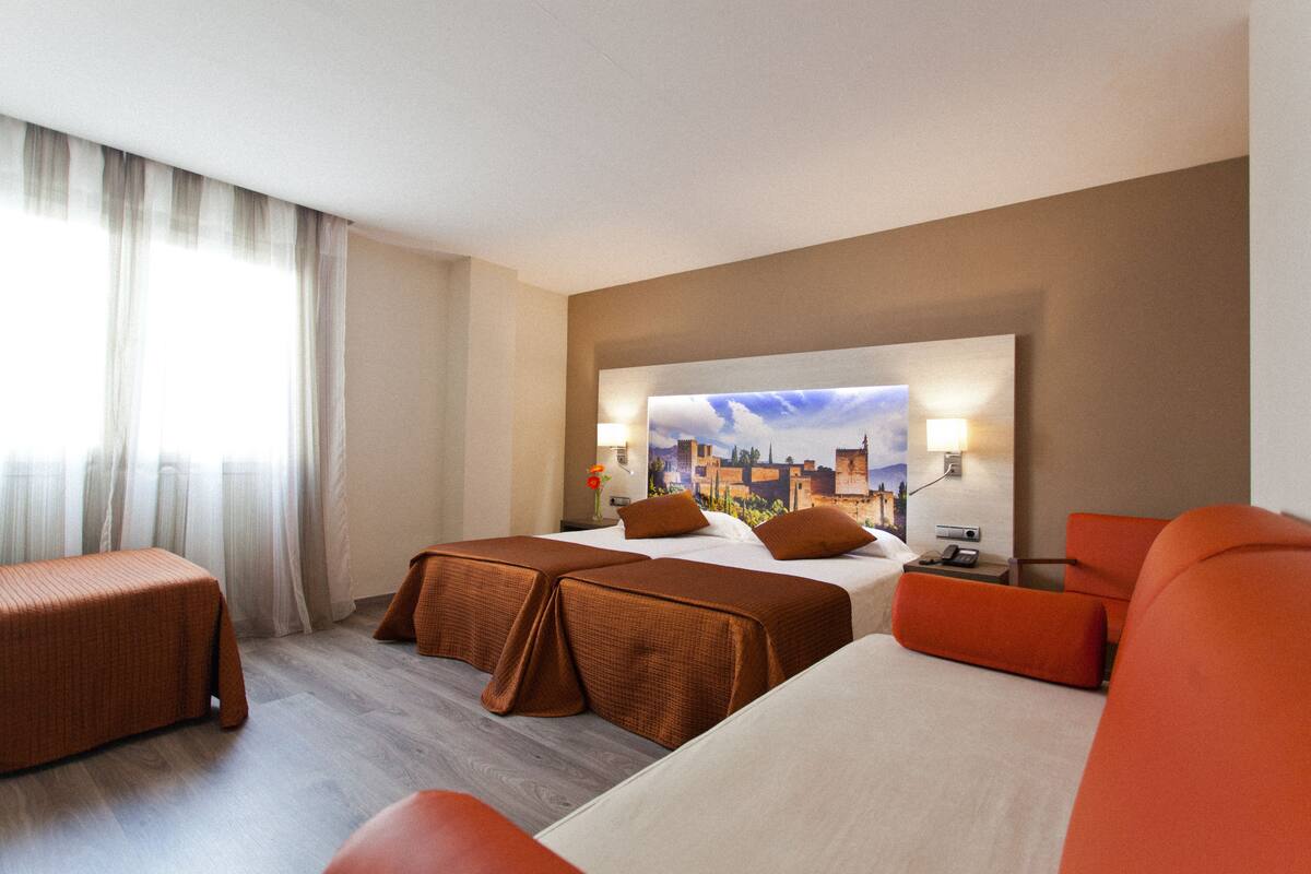 Habitación de hotel con dos camas, un sofá y un amplio ventanal con cortinas.