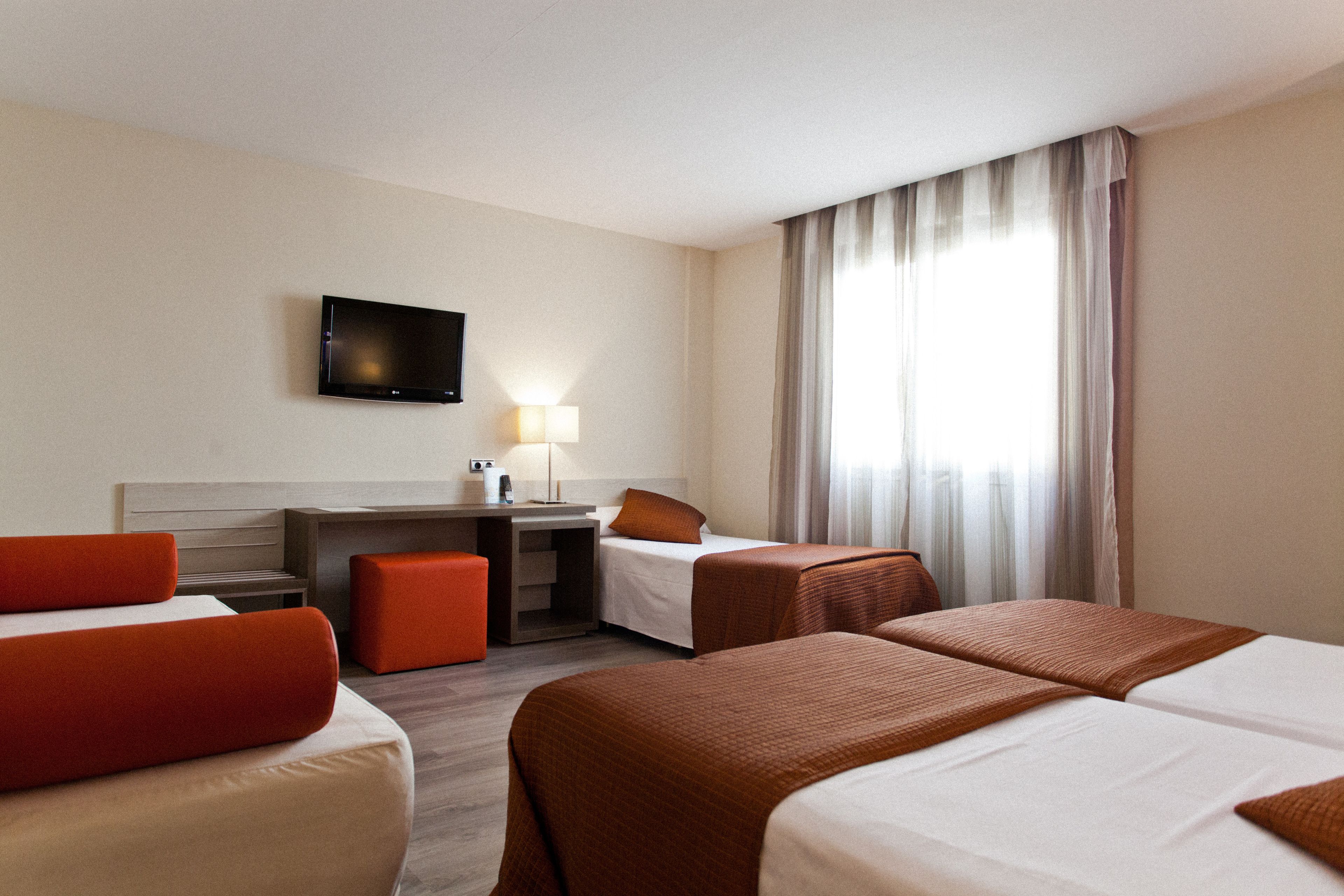A hotel room with two beds, a desk, a chair, a TV, and a window with curtains.