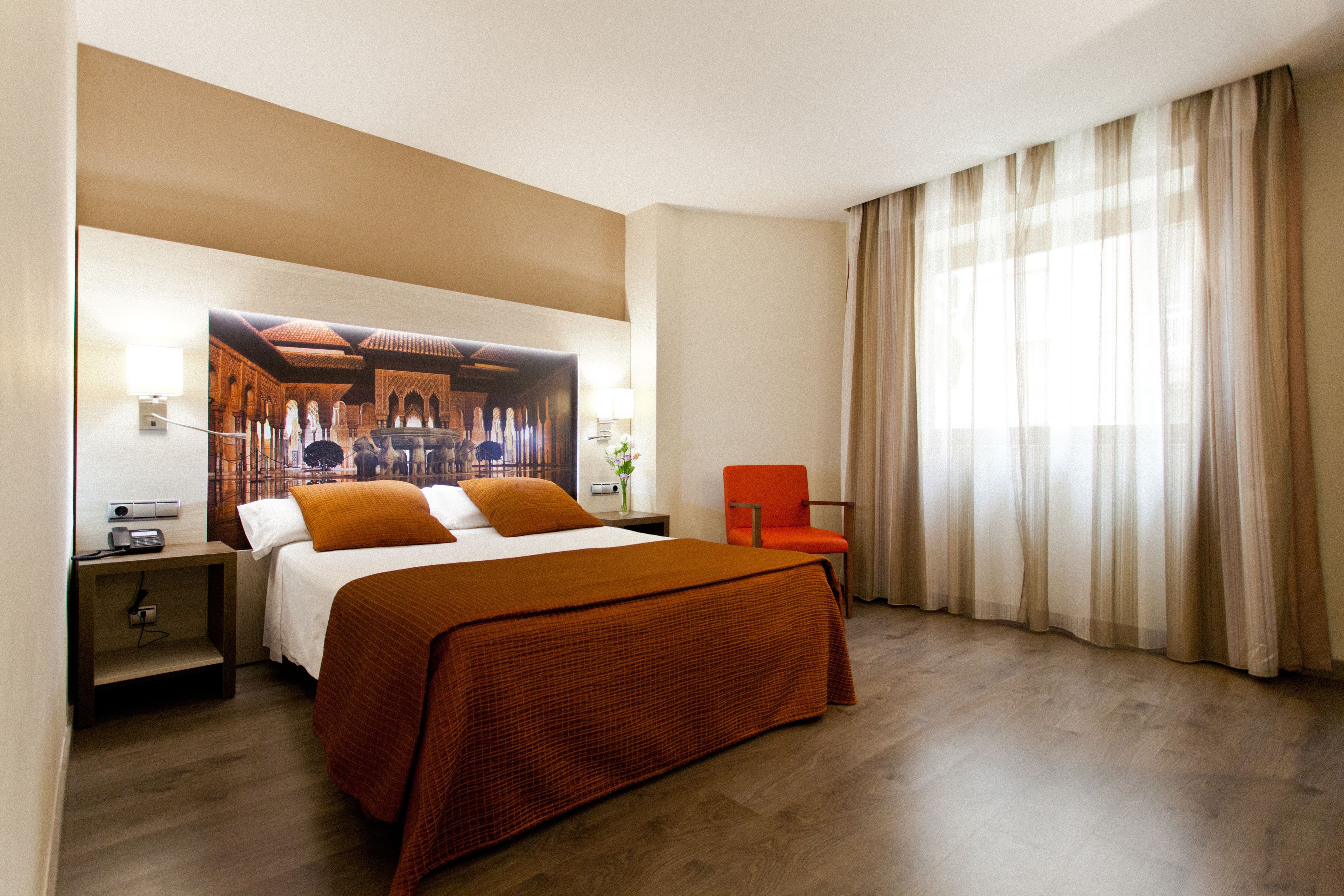 A hotel room with a large bed, a nightstand, a chair, and a window with curtains.