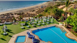 Un resort con piscina, tumbonas y vistas a la playa y al océano.