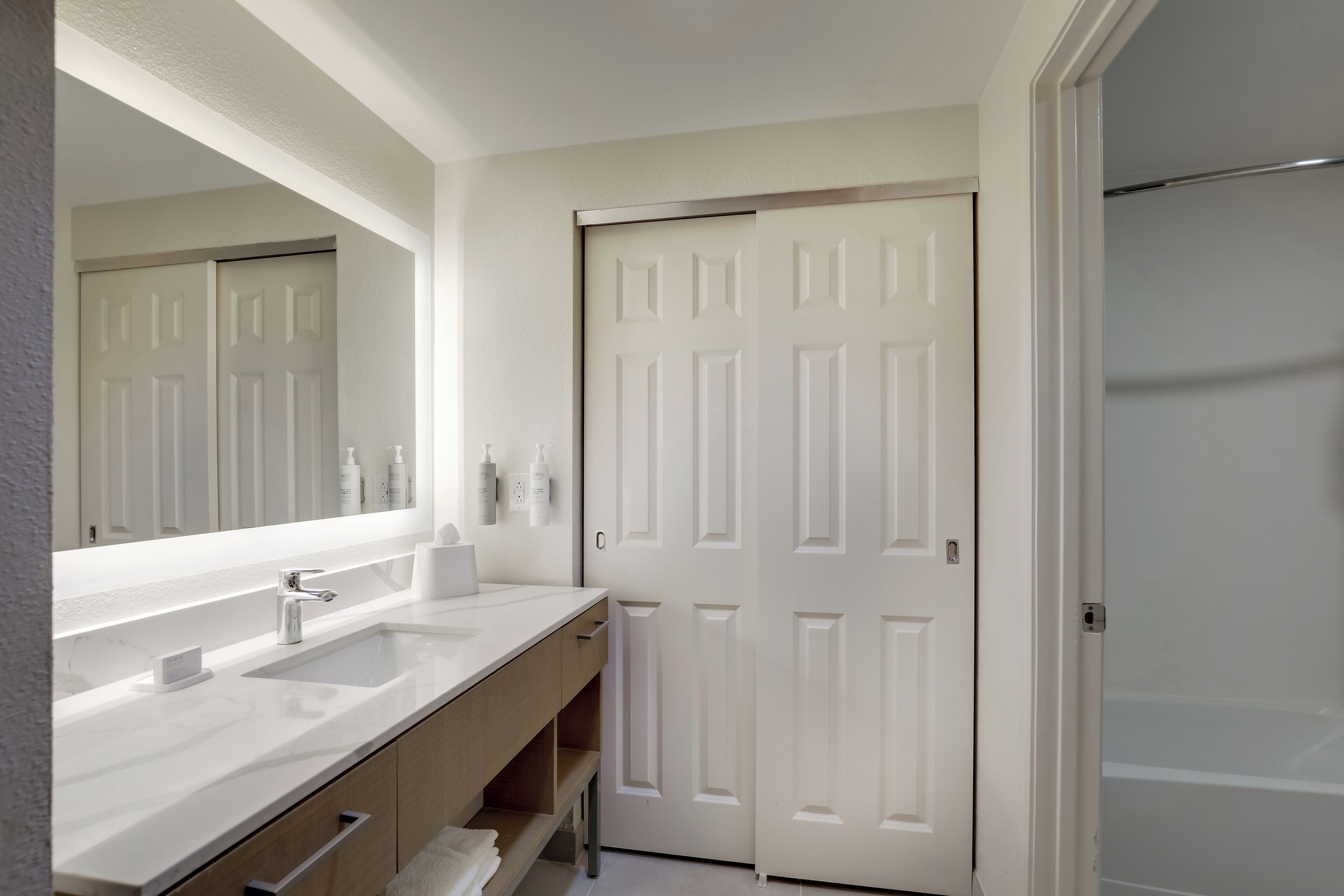 A modern bathroom with a double sink vanity, a large mirror, and a white door.