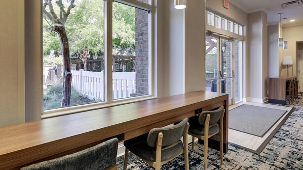 Un hall d’hôtel avec un comptoir d’accueil en bois, deux chaises, de grandes fenêtres donnant sur des arbres et une clôture blanche, ainsi qu’une moquette à motifs.