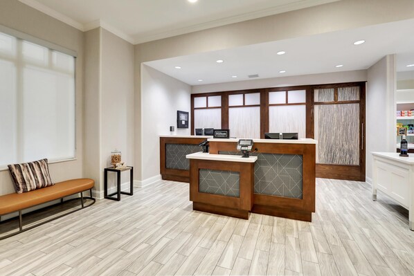 A reception area with a wooden reception desk, a bench, and a small table with a lamp.