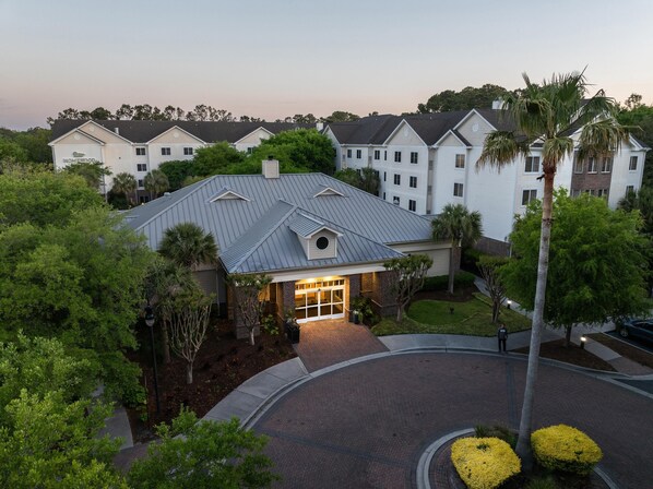 A residential building with a central entrance, surrounded by lush greenery and palm trees.