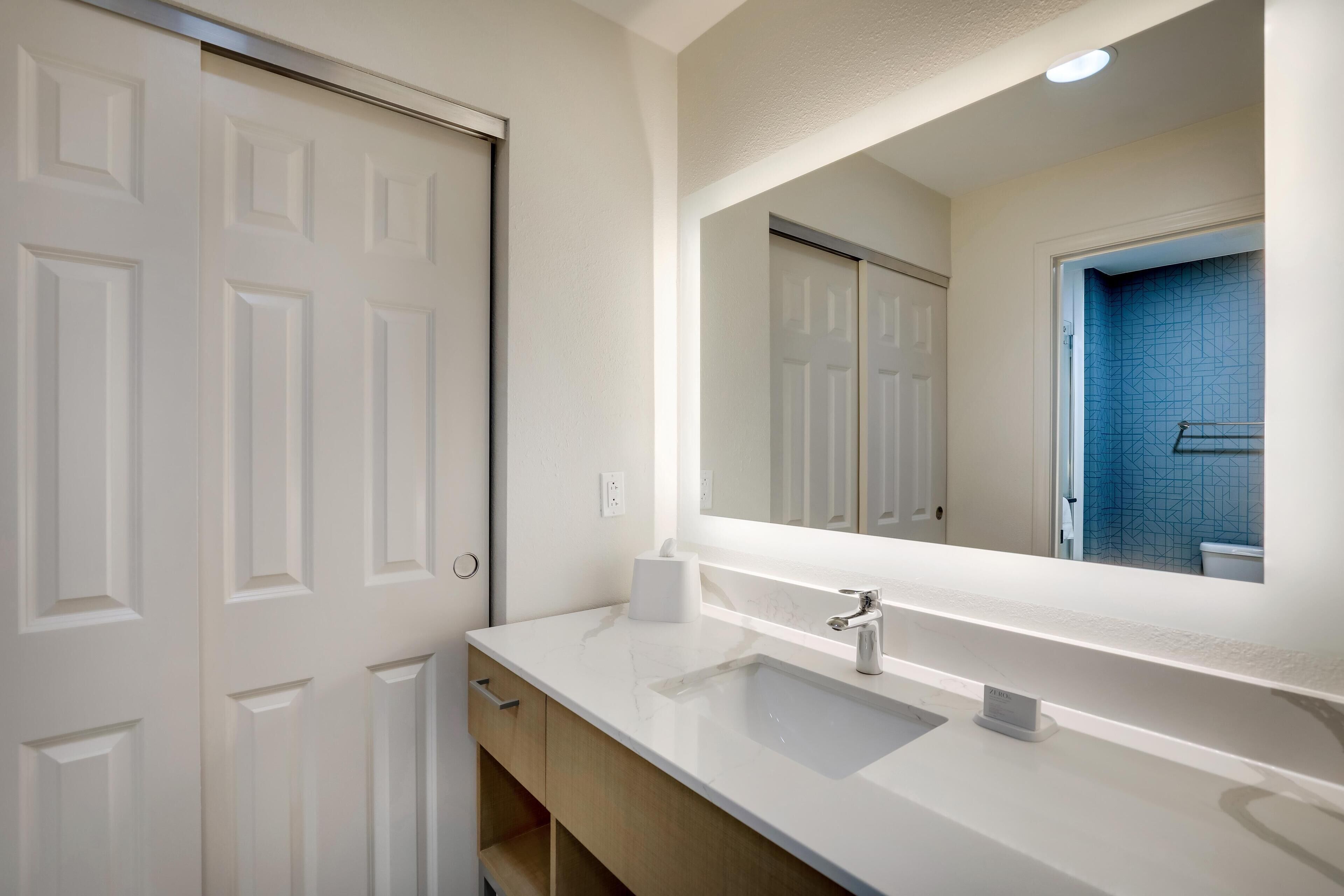 Un bagno moderno con un mobile lavabo bianco, un ampio specchio e una zona doccia rivestita di piastrelle blu.